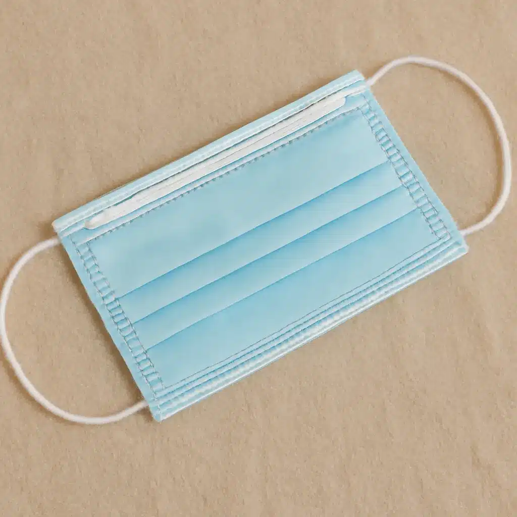 A blue disposable face mask with white ear loops placed on a beige surface.