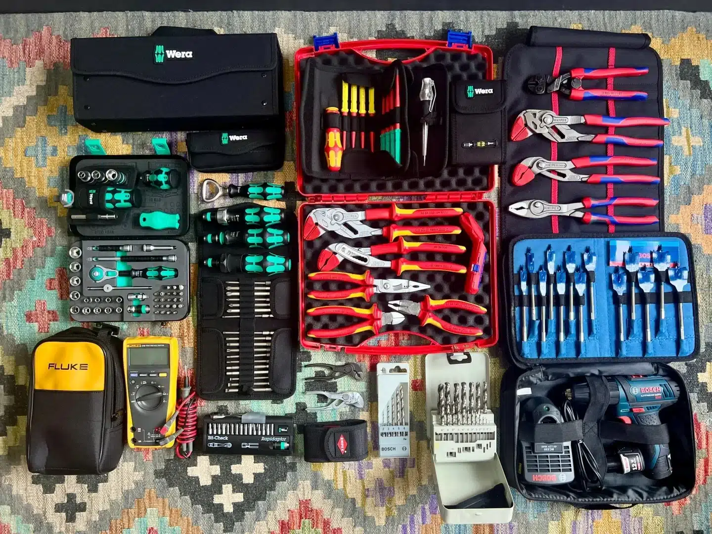 Various hand tools including screwdrivers, pliers, and drill bits organized in a grid on a colorful geometric rug.