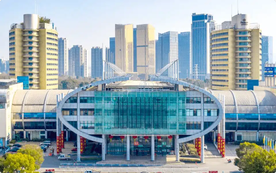 A modern exhibition center with a distinctive oval glass facade, surrounded by high-rise buildings in an urban landscape with clear skies.