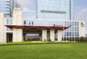 Modern hotel entrance with a red awning, large glass facade, and a landscaped garden in the foreground.
