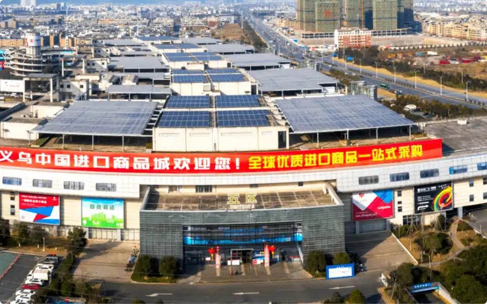 Large commercial building with banners and solar panels on roof, surrounded by parking and wide roads, viewed from above.