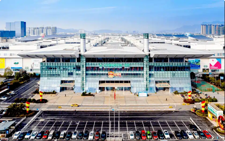 Front exterior view of a large convention center with a broad entrance, surrounded by parking and cityscape in the background.