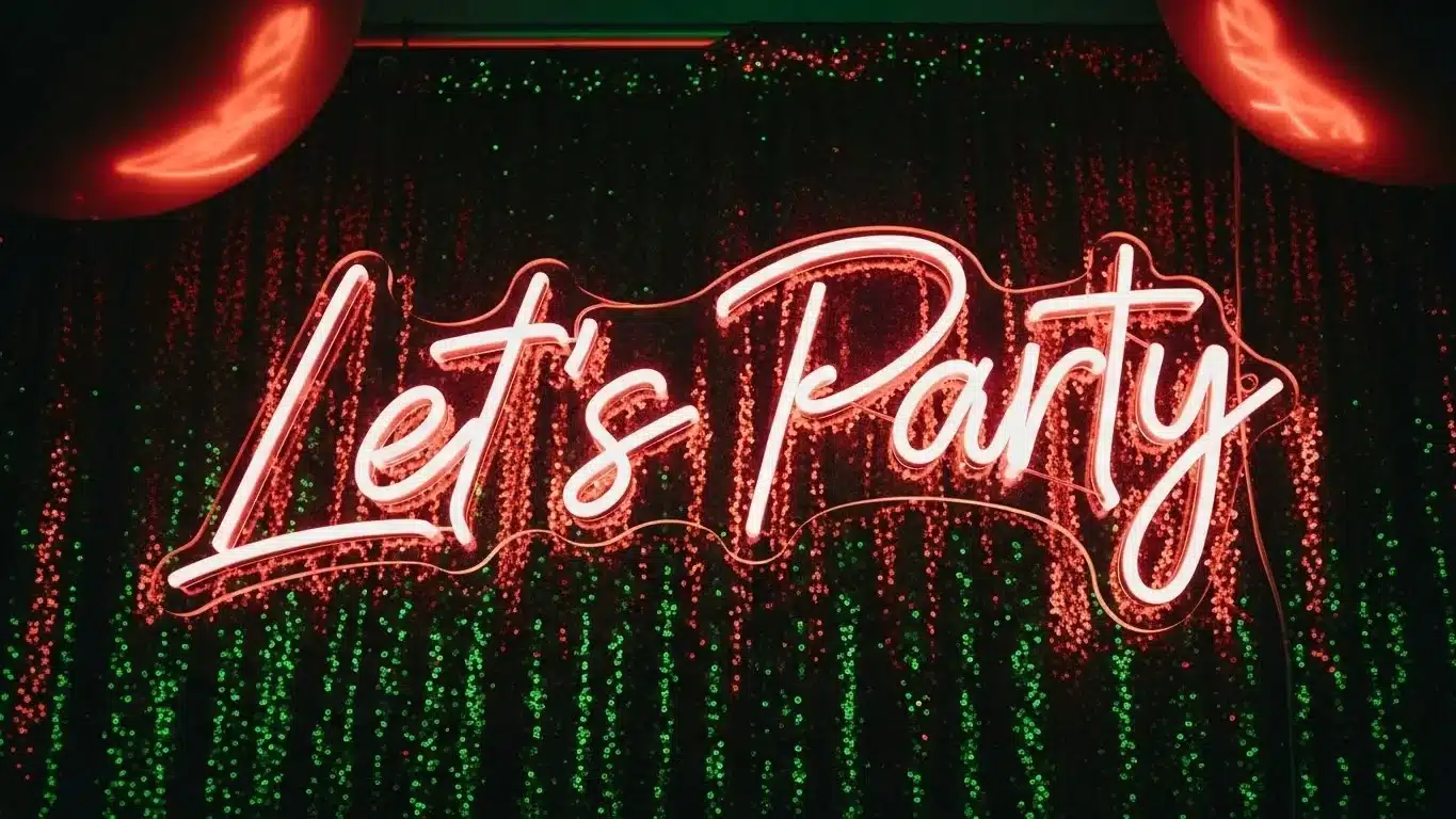 Bright red neon sign displaying 'Let's Party' on a dark background with green glittering curtain, creating a festive atmosphere.