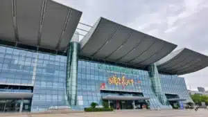 Modern glass-covered exterior of a convention center with large overhanging roof and signage, under a cloudy sky.