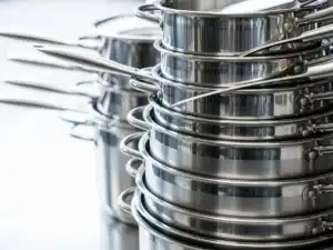 Neatly stacked stainless steel pots and pans with visible handles in a bright kitchen setting.
