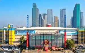 Yiwu International Trade Market entrance with modern skyscrapers in the background and busy area in front, clear blue sky overhead.