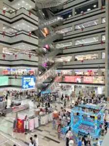 Interior de centro comercial movimentado com vários níveis, com escadas rolantes, expositores de lojas e vários clientes a explorar os diferentes níveis.
