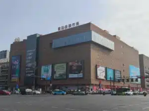 Large shopping center with a modern exterior featuring advertisements on the facade and various vehicles at the intersection.
