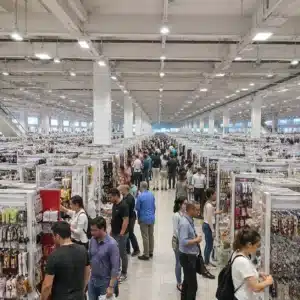 Hyper-realistic wide-angle photography of Yiwu Market interior, thousands of small product booths stretching into distance, bright fluorescent lighting, mixed crowd of Chinese and Western buyers examining goods, clean aisles, no text, no brand logos, professional commercial photography style, shot on Phase One XF IQ4, f/8, ISO 100